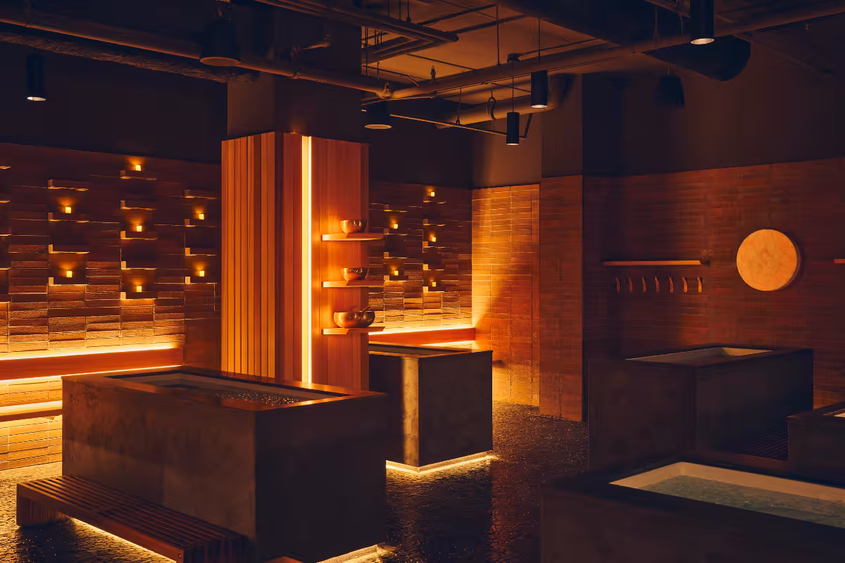 Warm-lit modern spa room with brick walls, water basins, wooden benches, and soft ambient lighting.