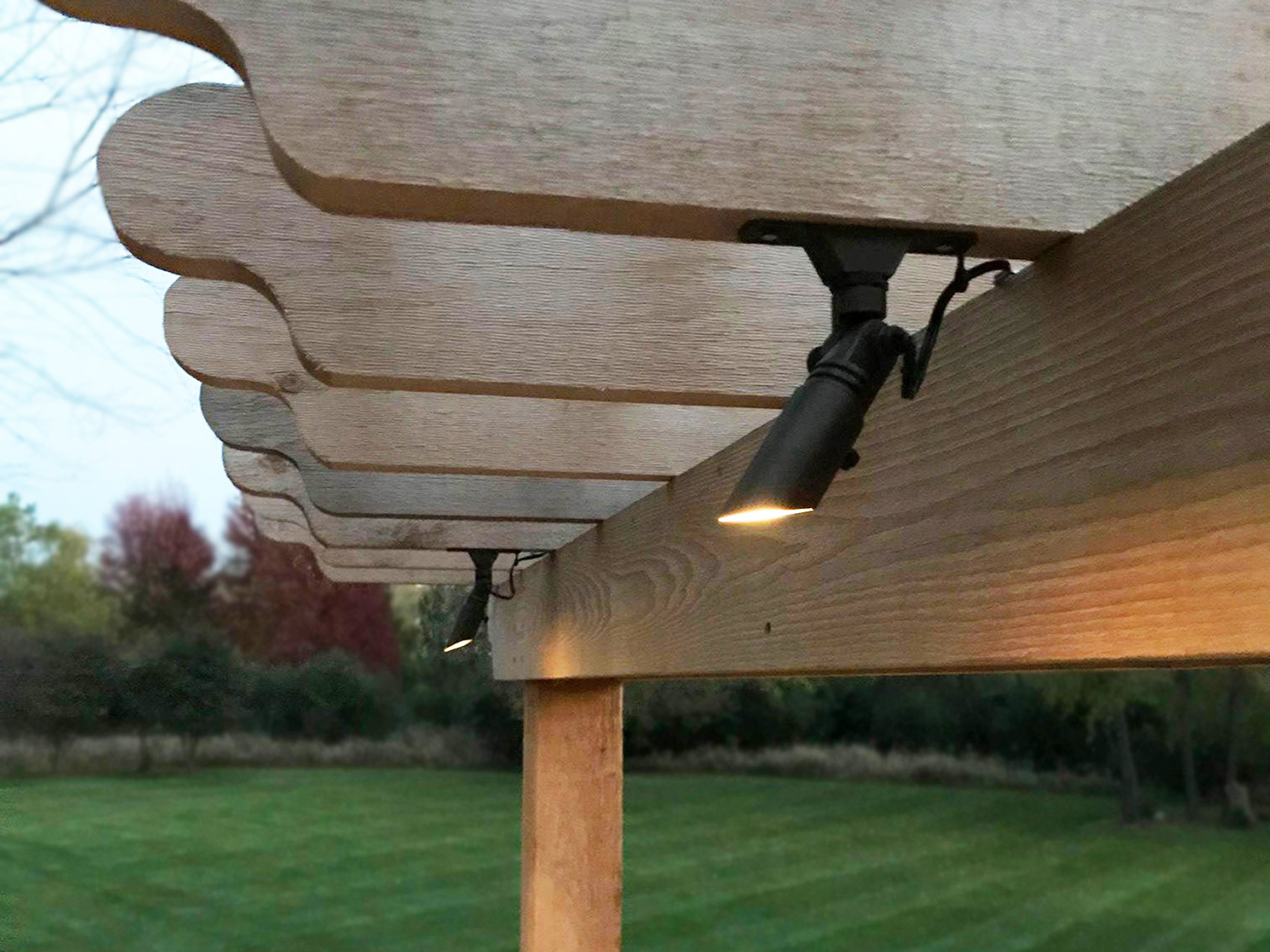Black downlight mounted under a wood pergola beam casting soft light on the patio below