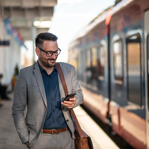 A business professional standing outside of a train smiling down at his phone