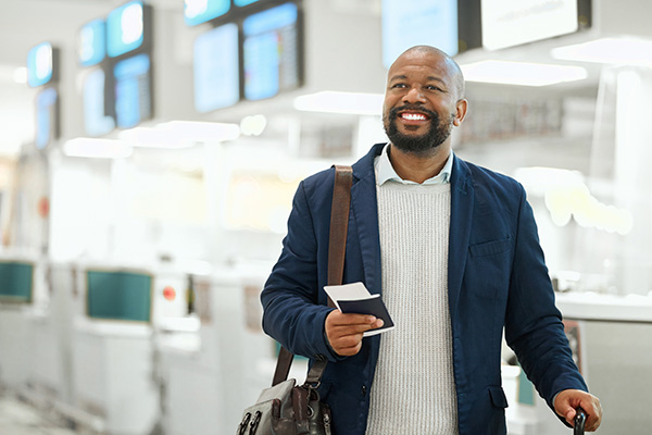 A business professional standing in an airport smiling while holding his passport.