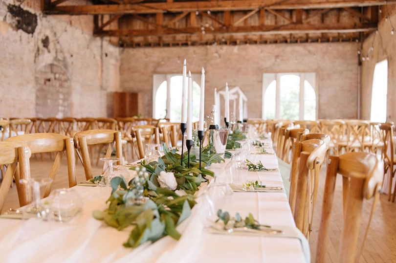 view down long table decorated for a wedding with candles greenery and cross-back chairs in a brick loft wedding venue