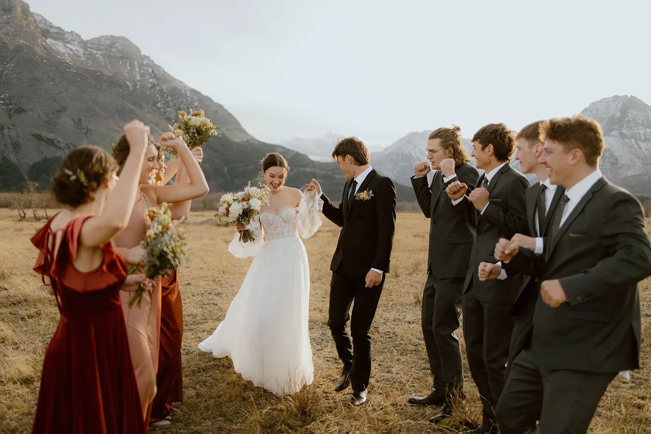 Bridal party dancing and cheering for bride and groom in Waterton Lakes National Park with mountain view in the background
