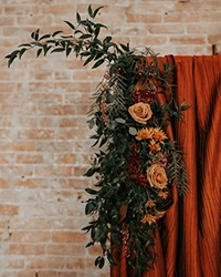 fabric and greenery draped copper arch against brick background