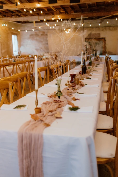 Long decorated wedding table with candles and a blush table runner in brick loft venue.