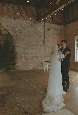 Bride and groom dancing in a rustic spacious loft room with brick walls and string lights.