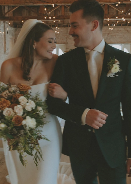 Bride and groom smiling at each other while walking arm in arm indoors during their wedding.