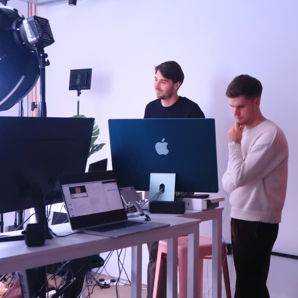 Two men in a room with a laptop and a monitor.
