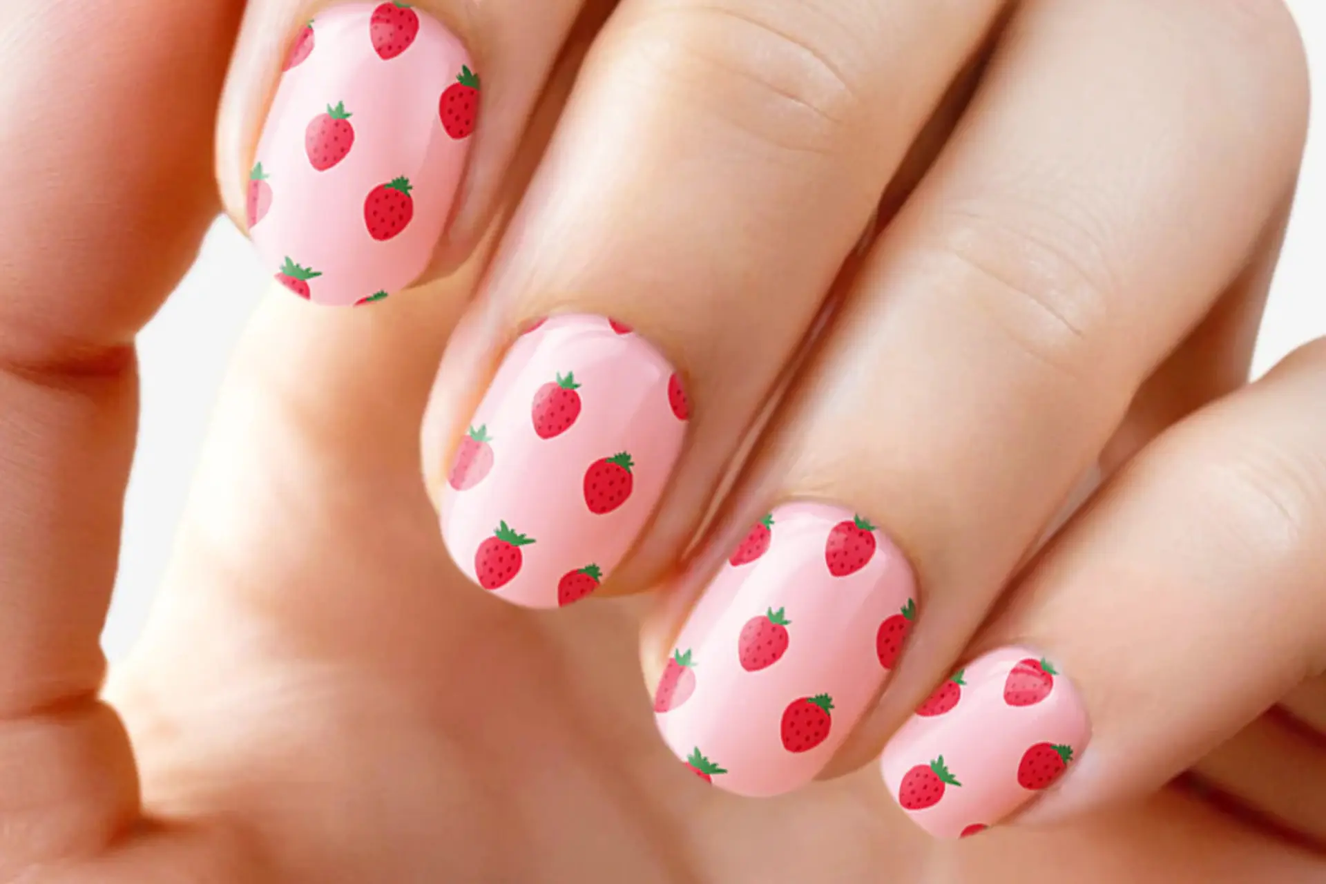 A hand with a pink nail polish with a strawberry design.