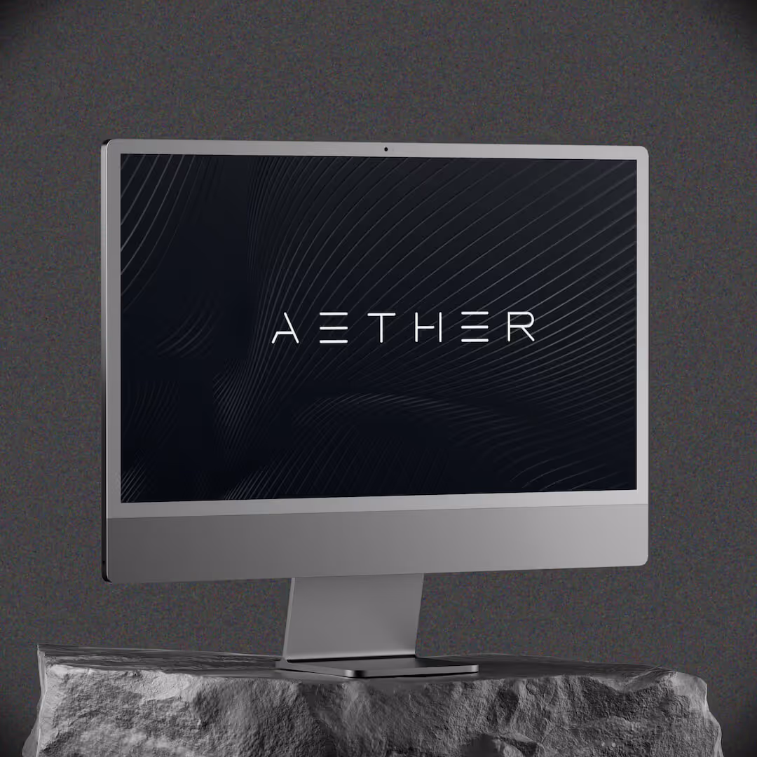 Modern silver desktop computer on a textured stone surface with a dark screen displaying the word AETHER in stylized white text.
