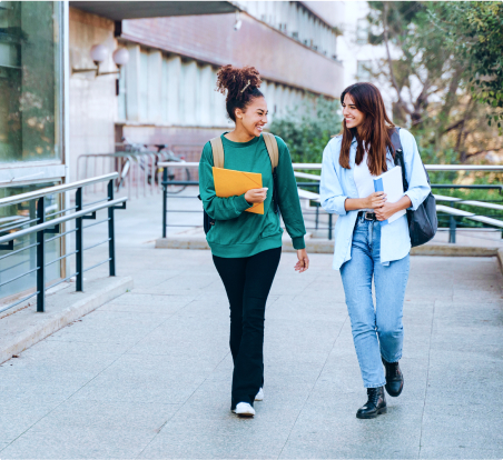 Two young females walking on campus and smiling at each other.