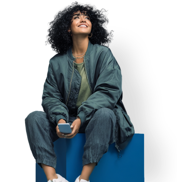 Young woman with her mobile phone in her hands and sitting on a box. She is looking up and smiling.