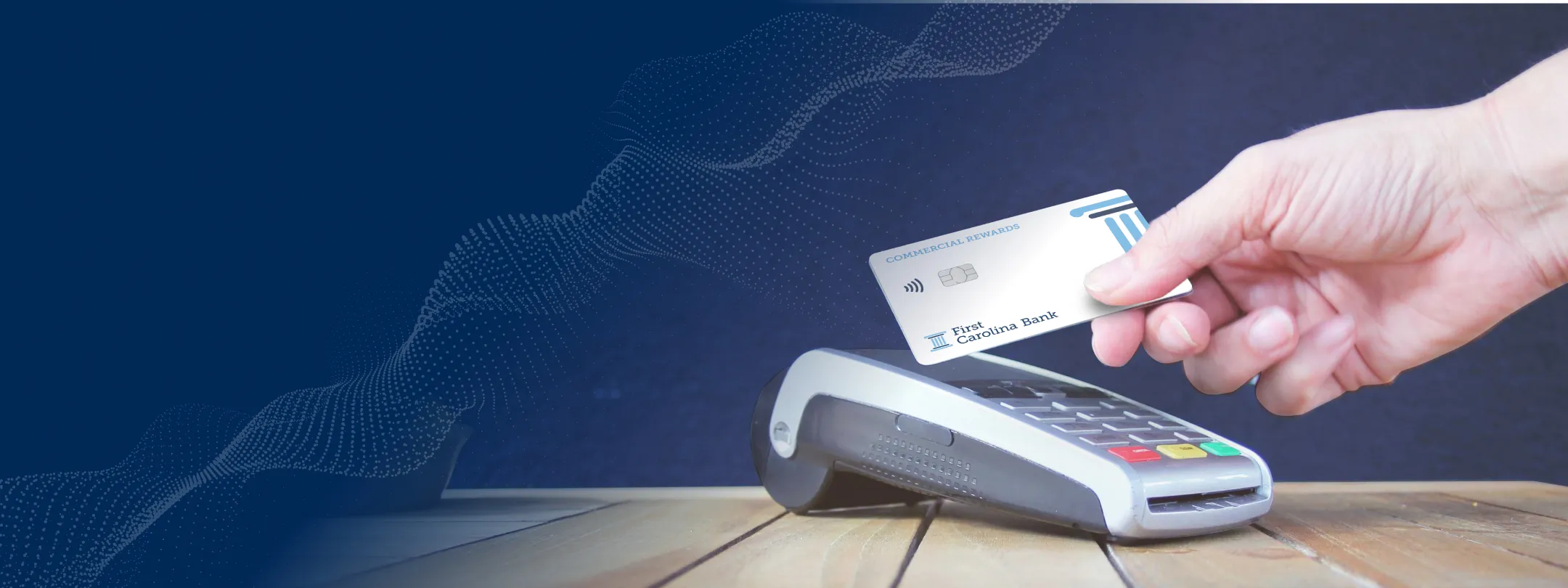 A hand hold a debit or credit card and tapping it against an EMV chip reading device.