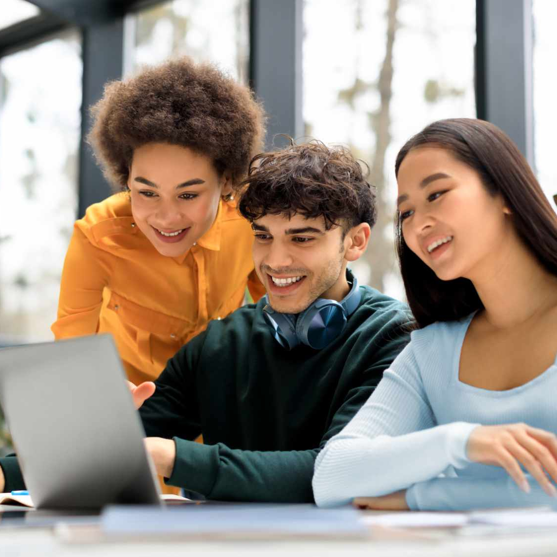 Happy international students looking at laptop screen and smiling