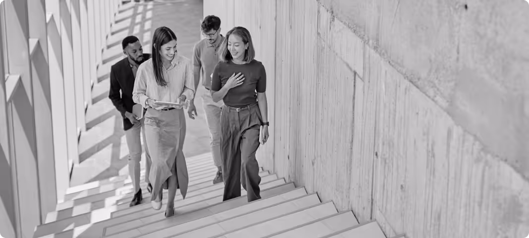 Four young professionals walking up stairs inside a modern building, engaged in conversation and smiling.