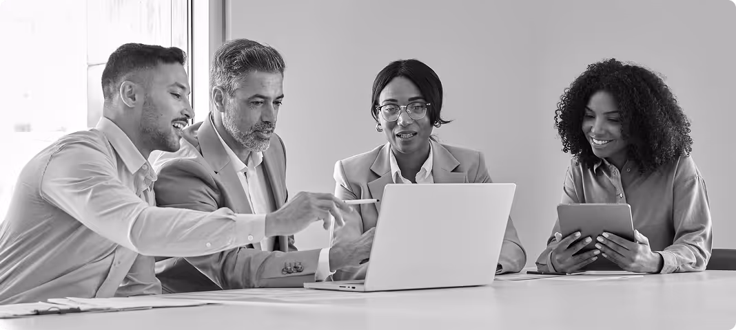 Four business professionals collaborating around a laptop and tablet in a modern office.
