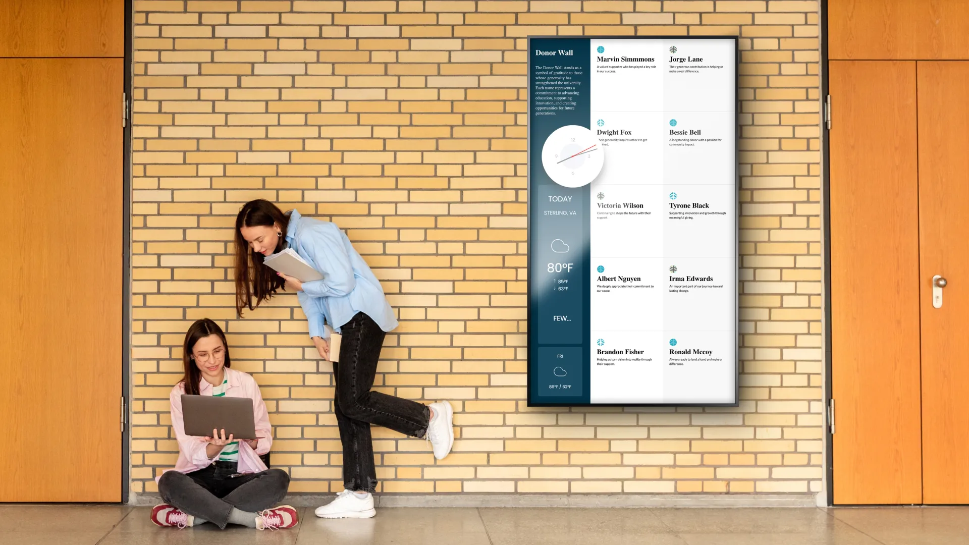Two students beside a portrait style digital donor wall.