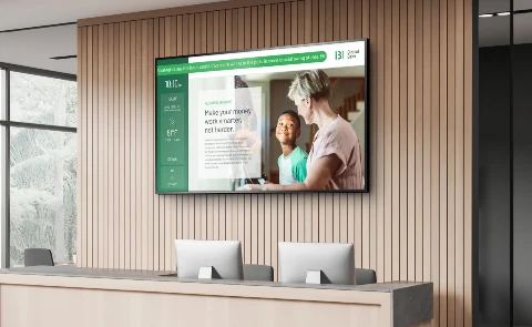 A modern office reception area features a large screen displaying financial tips, with two people engaged in conversation nearby.