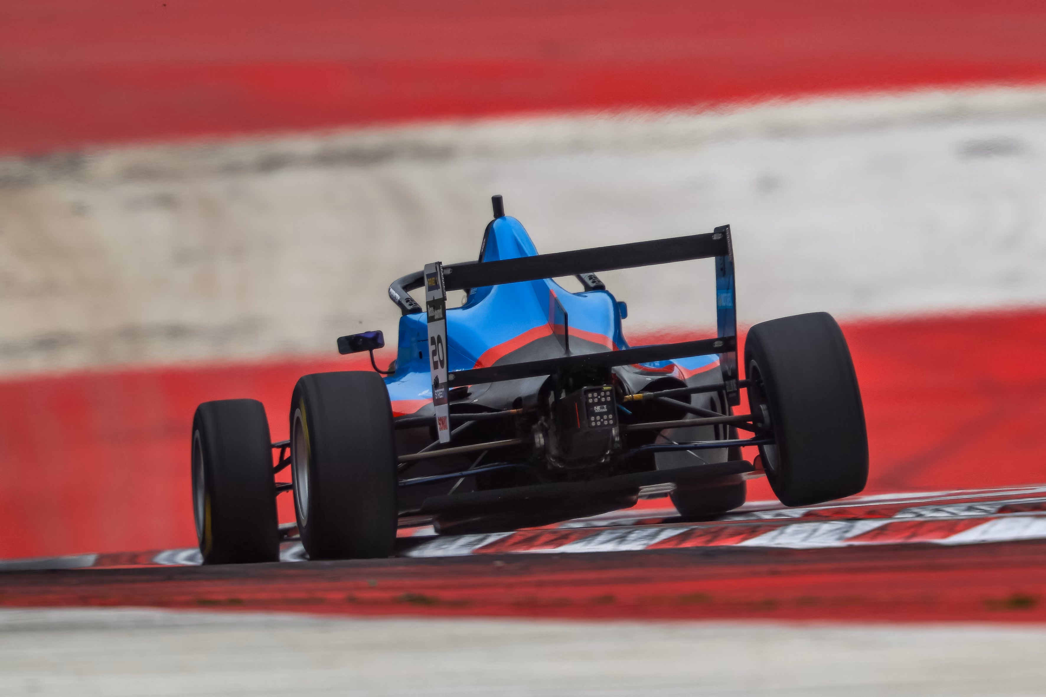 Rear view of Elia Weiss F4 race car speeding on a red and white curbed race track.