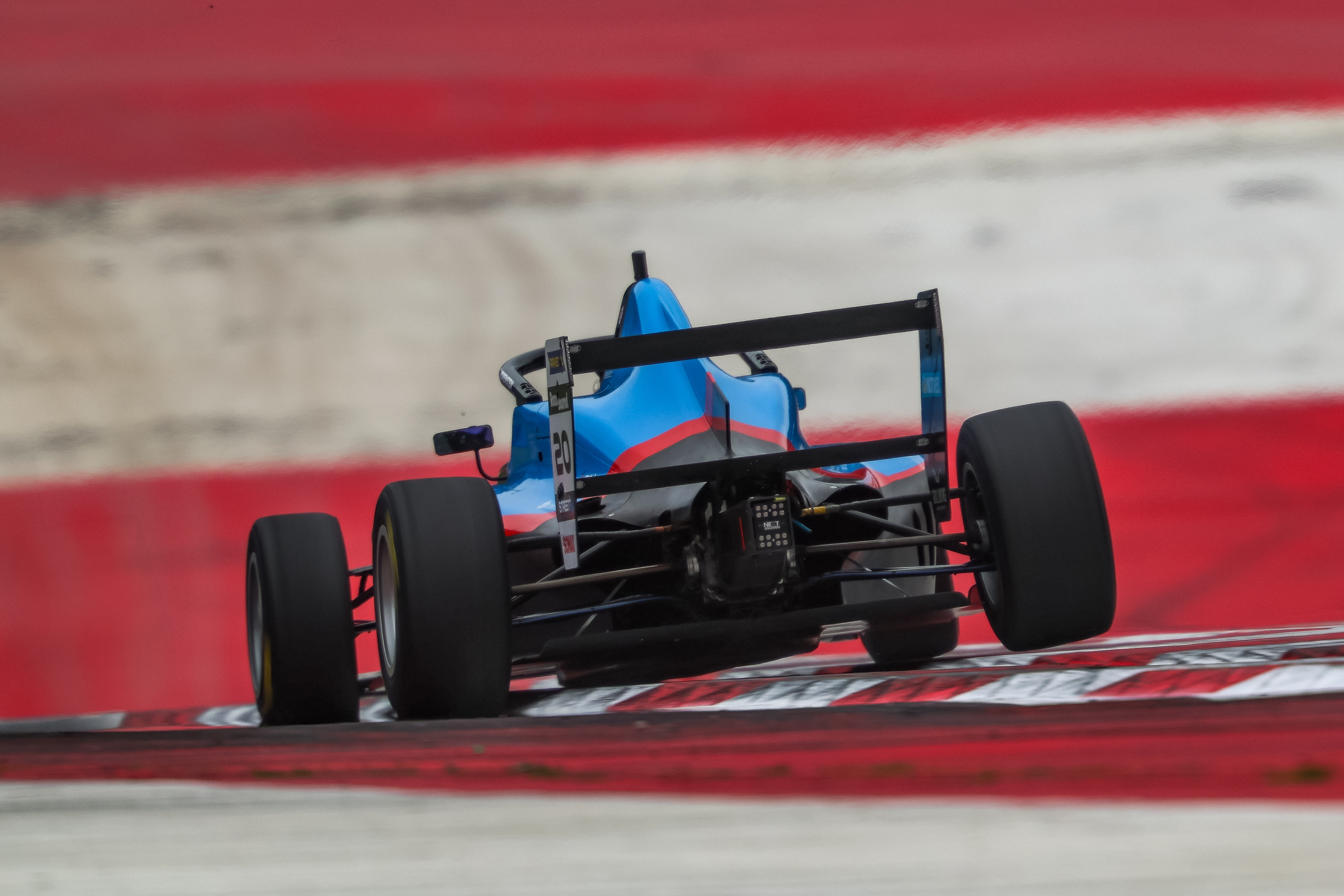 Rear view of Elia Weiss F4 race car speeding on a red and white curbed race track.