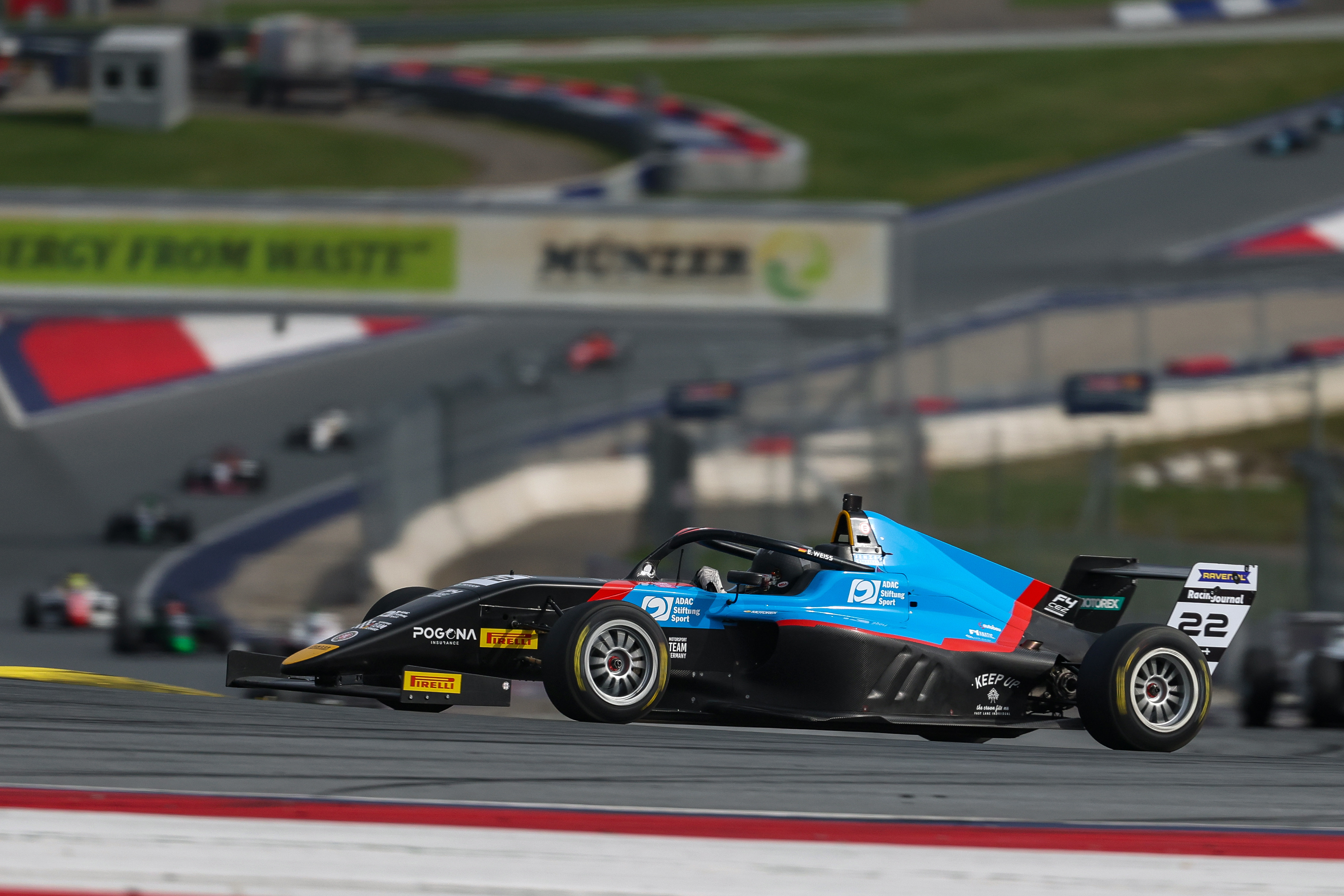 Elia Weiss's open-wheel race car number 22 on a racetrack with other cars blurred in the background.