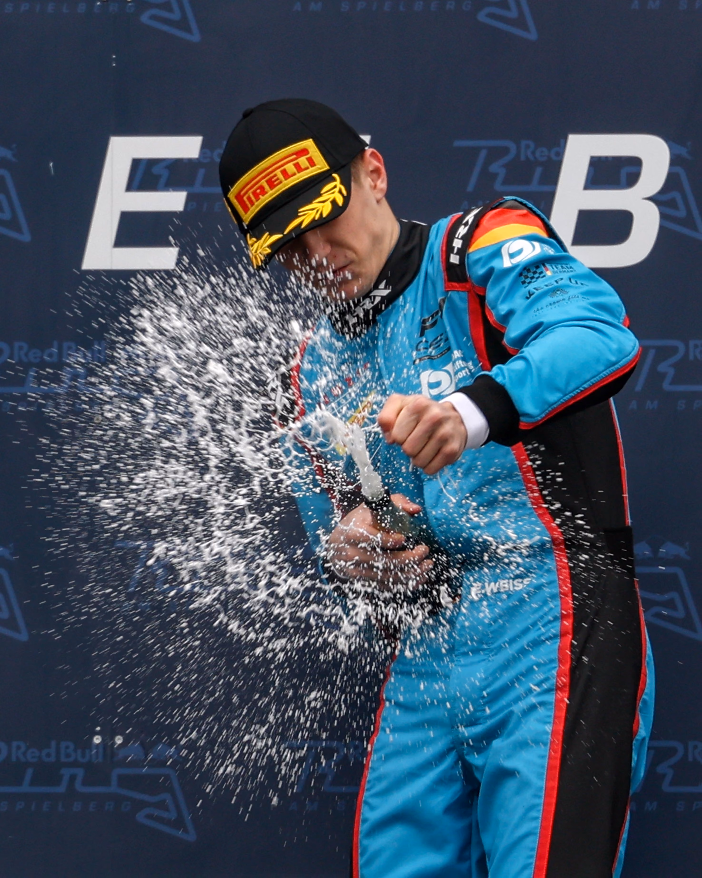 Elia Weiss in blue and black suit with Pirelli cap spraying champagne in celebration.