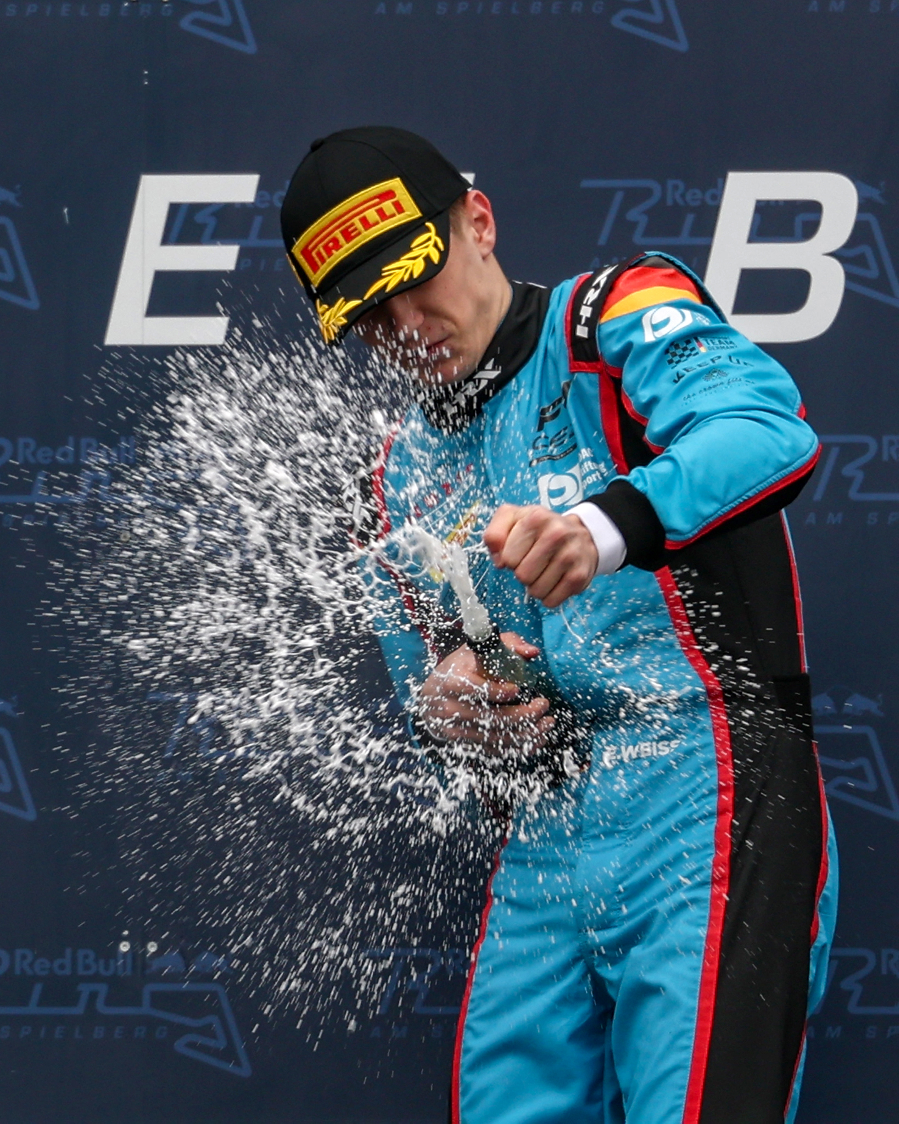 Elia Weiss in blue and black suit with Pirelli cap spraying champagne in celebration.
