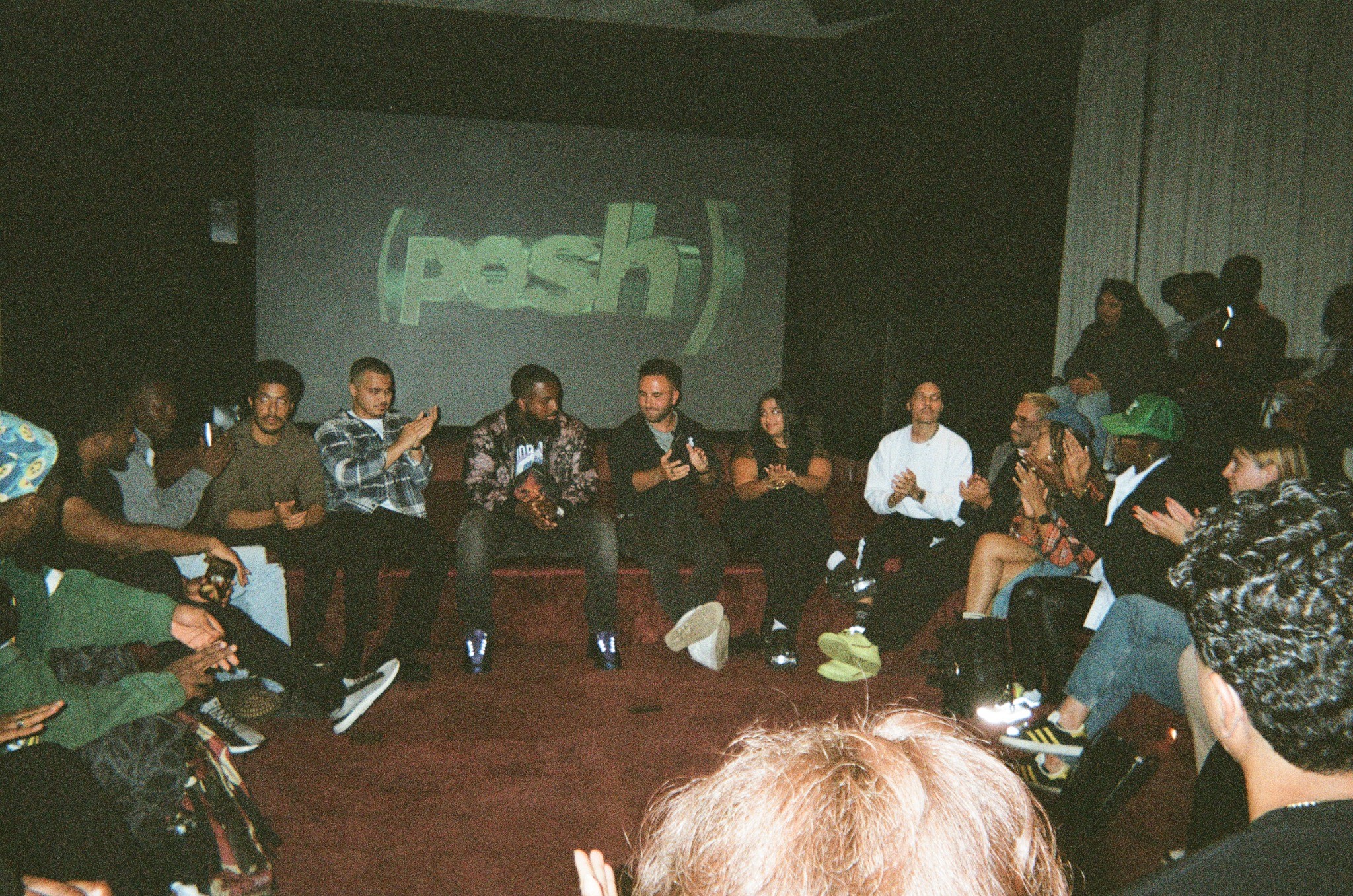 Group seated on couches before a screen reading 'posh' in a dim lounge