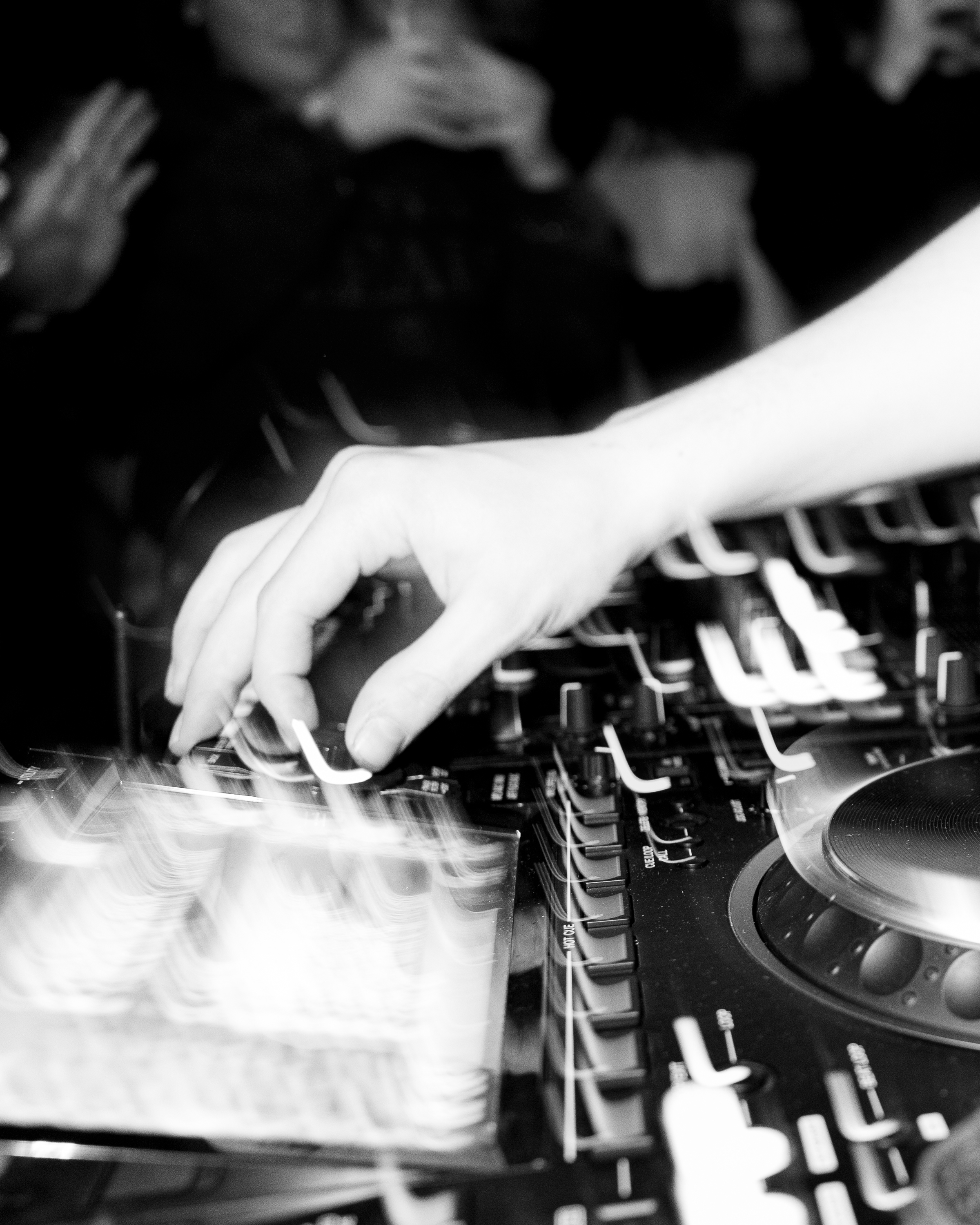 Black-and-white close-up of a hand adjusting the faders on a DJ mixer