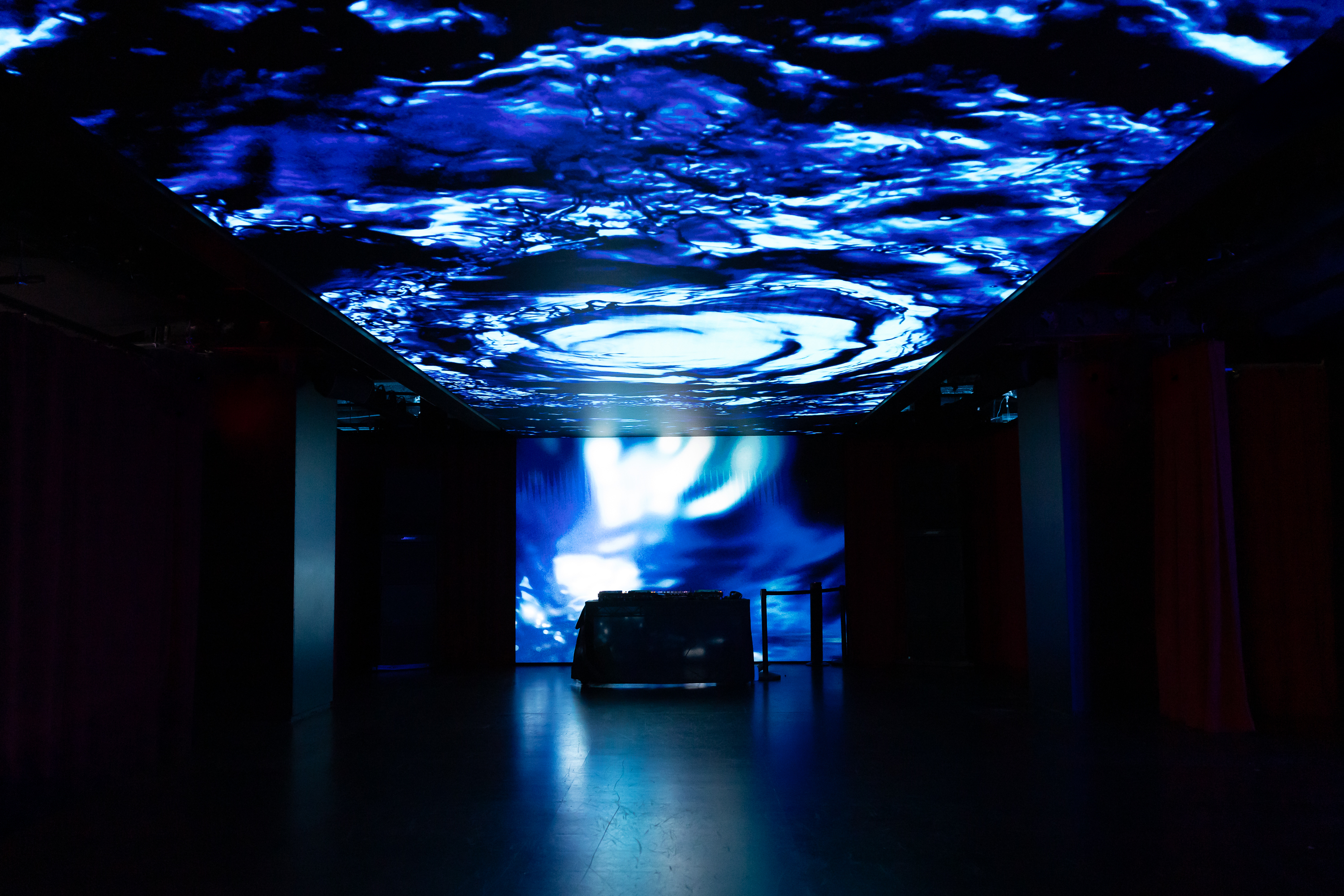 Dark venue with rippling blue water visuals projected across the ceiling