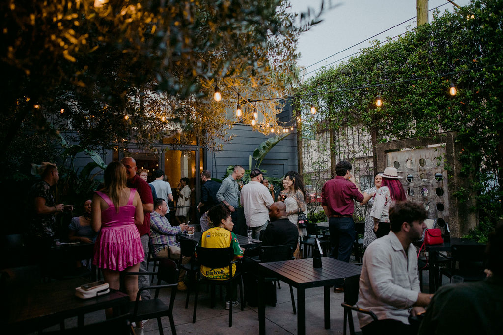 Guests mingling at dusk on a string-lit outdoor patio surrounded by greenery