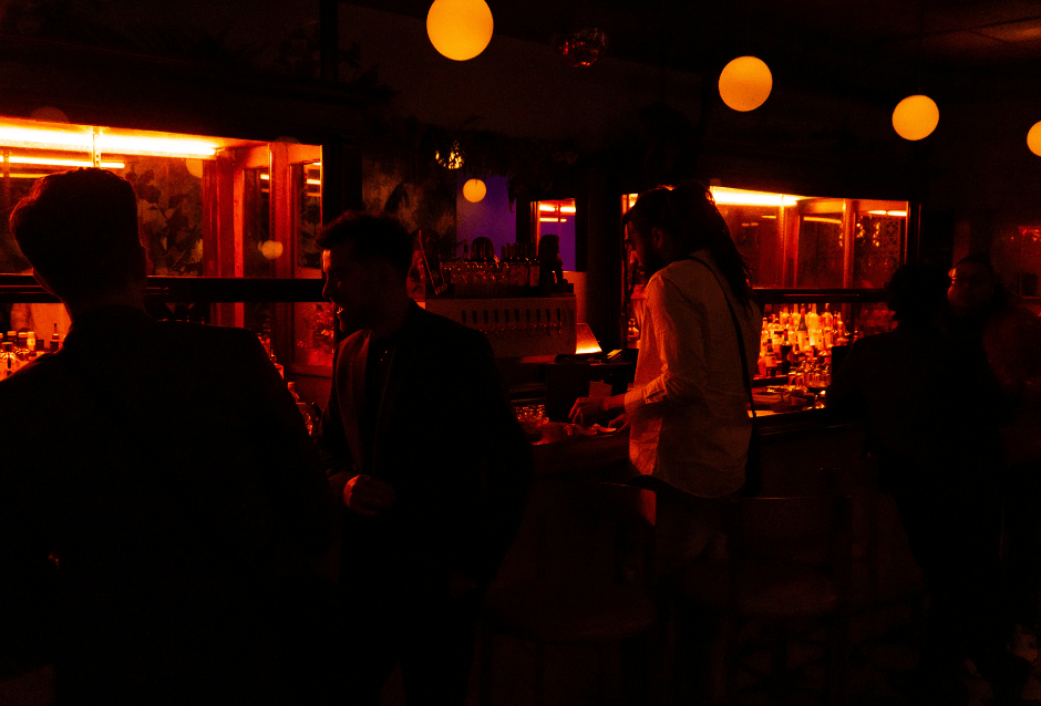 Patrons gathered at a bar under warm red lighting and hanging globe lamps