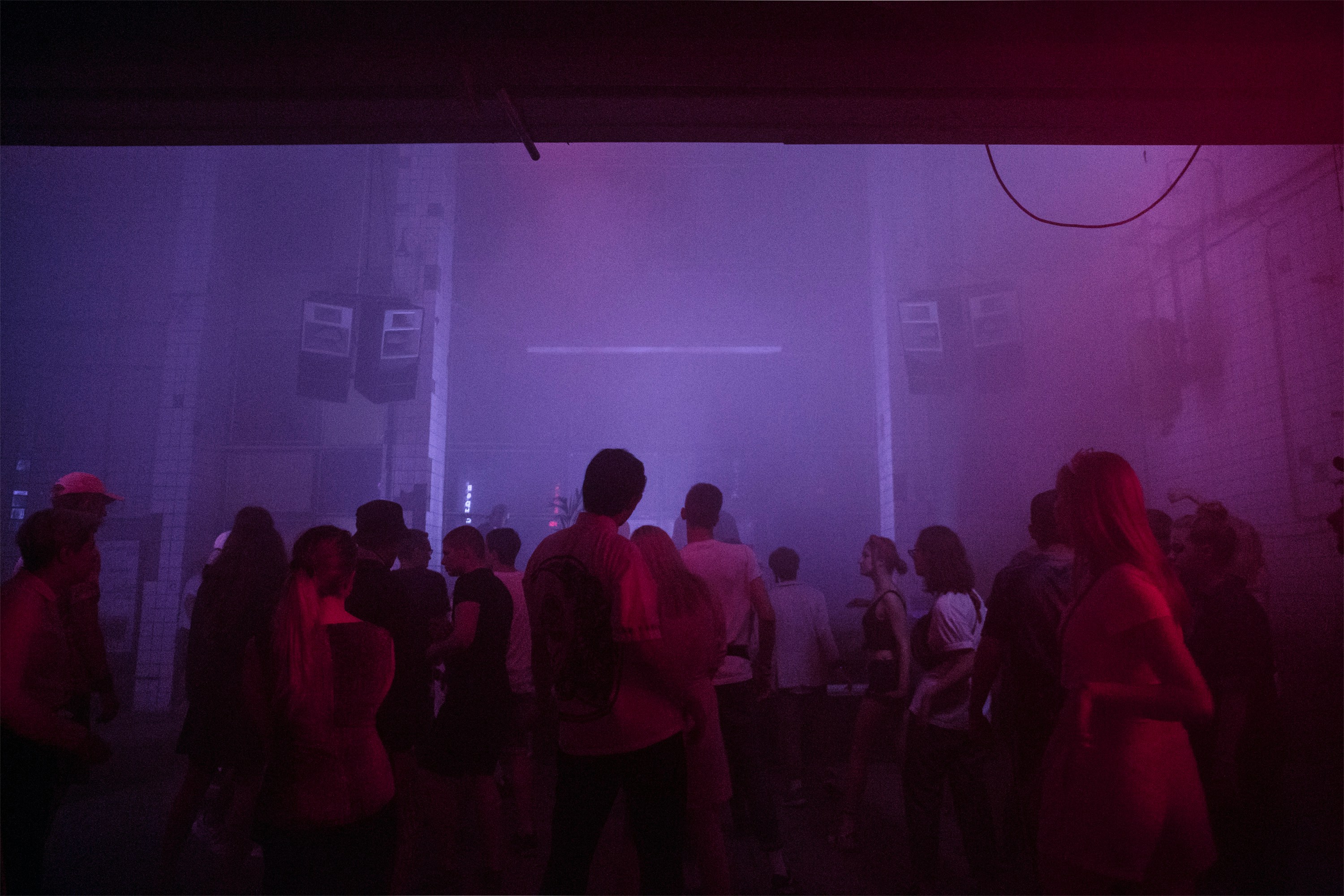 Crowd dancing in a smoky warehouse rave under purple and pink lighting