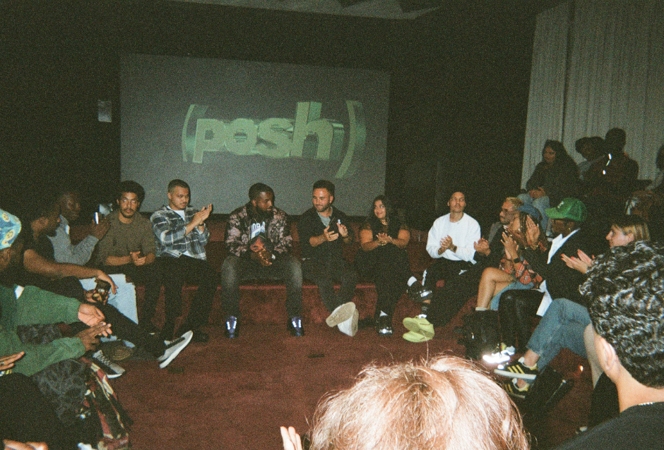 Crowd seated in a circle at an intimate event, lit Posh logo projected on the wall