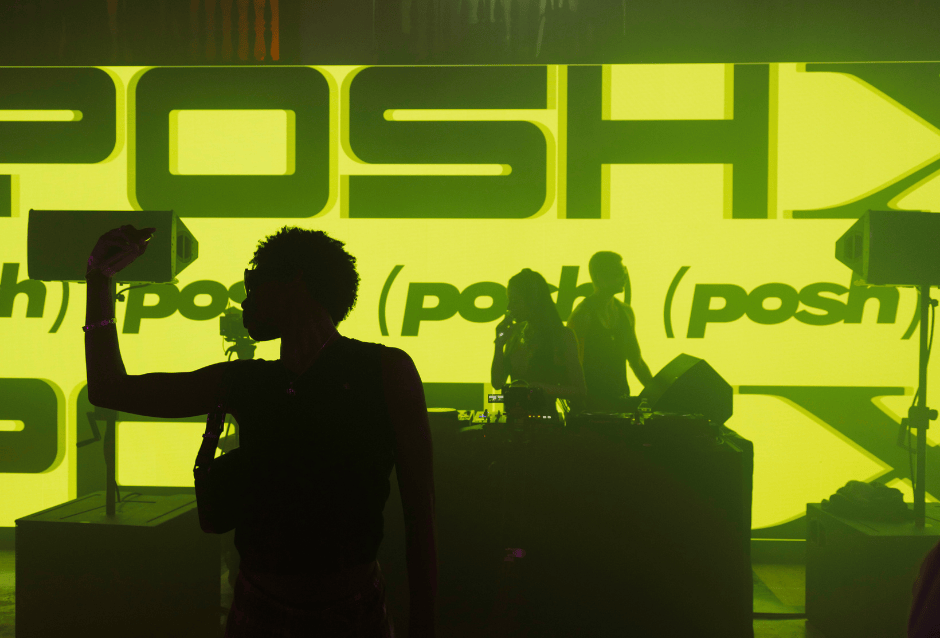 Silhouetted crowd before a stage backlit by glowing green Posh logos