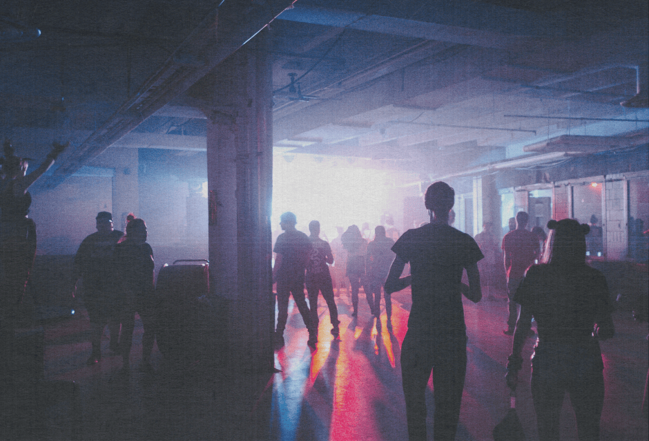 Silhouetted people walking through a hazy, dim industrial warehouse space