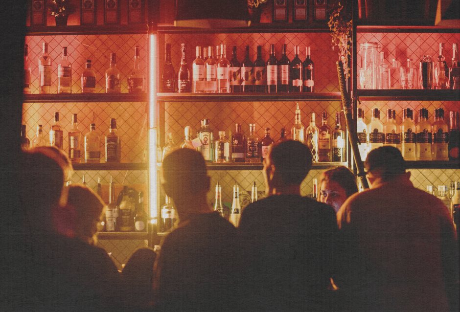 Crowd silhouetted in front of a red-lit, well-stocked backlit bar