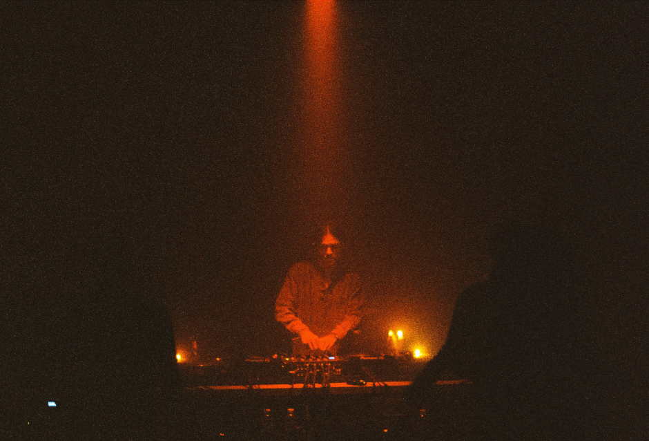 DJ performing in darkness under a single beam of warm light