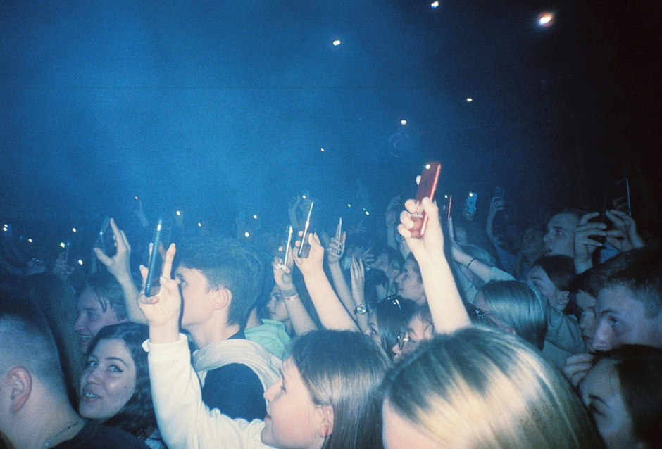 Dense concert crowd with raised hands and phones under blue stage haze