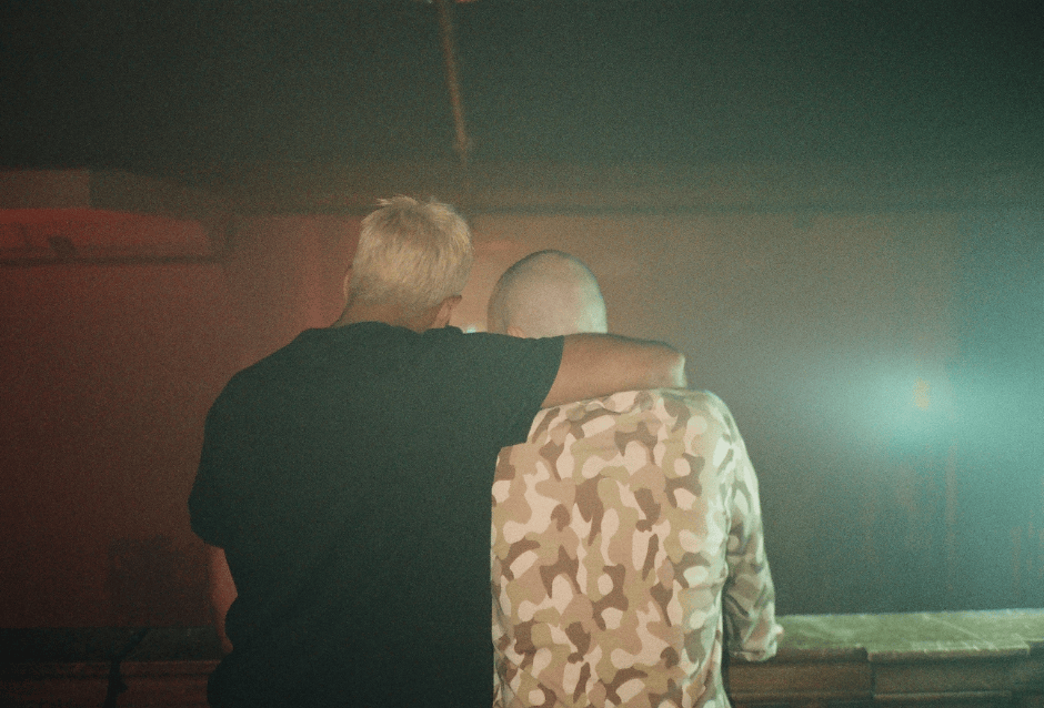 Two people embracing from behind in misty pink and teal lighting