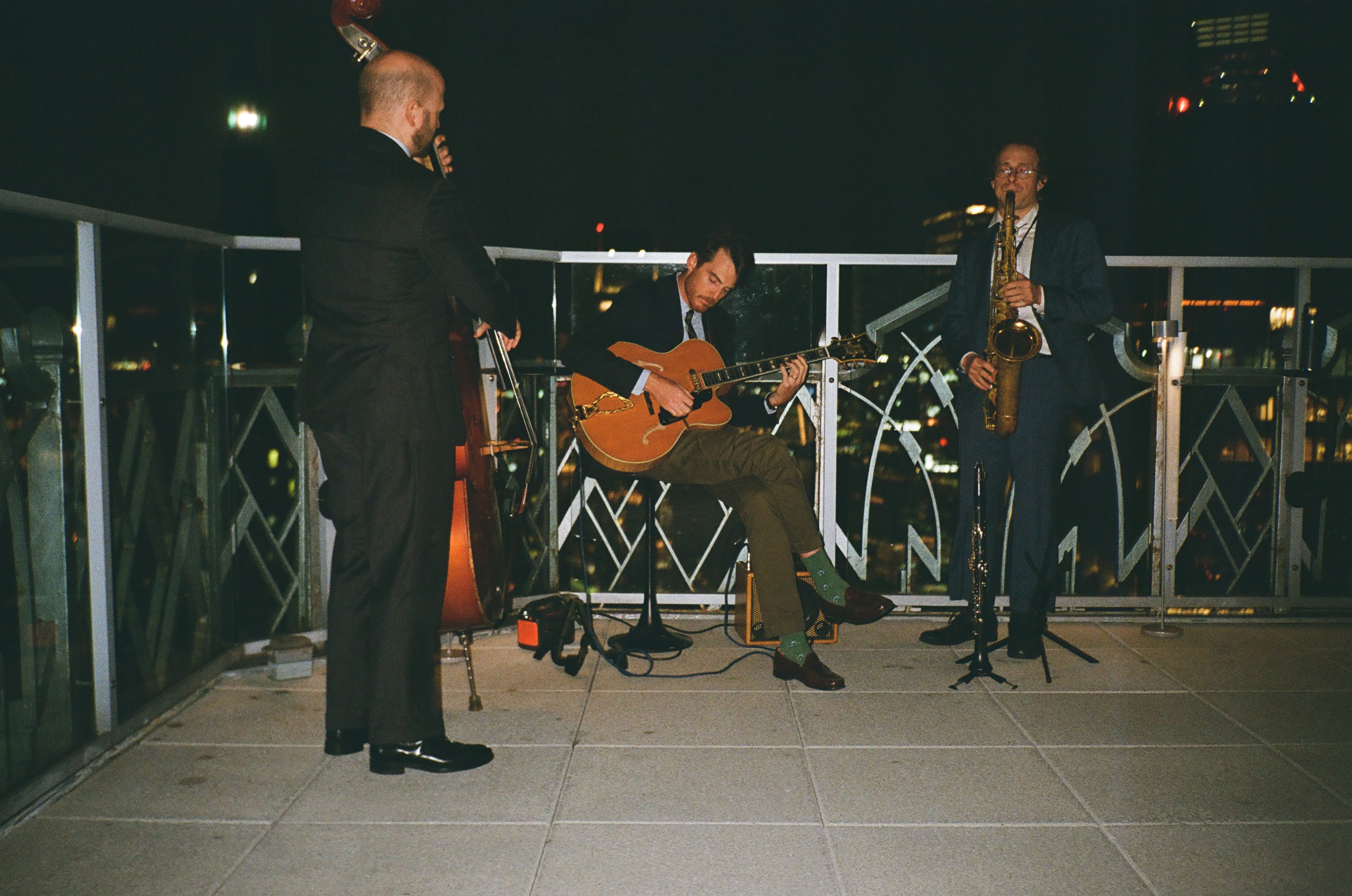 Jazz trio with bass, guitar and saxophone playing on a city rooftop at night