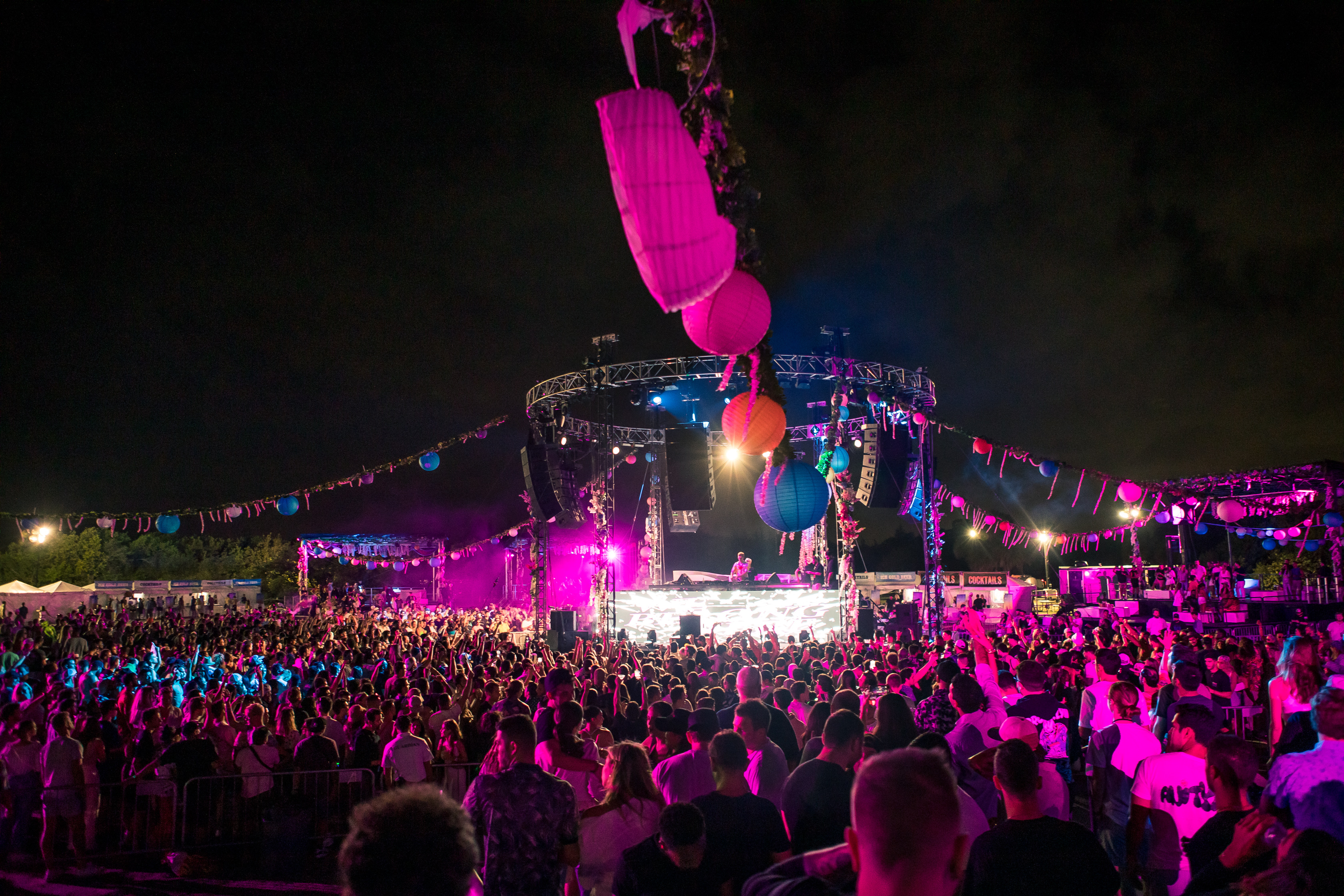 Nighttime festival crowd dancing under pink stage lights and hanging paper lanterns