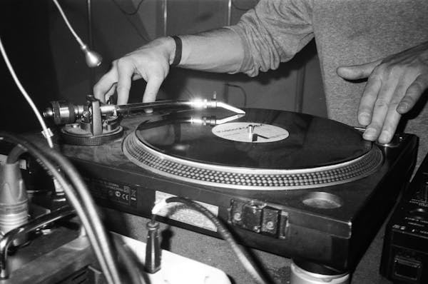 Black-and-white close-up of hands cueing a vinyl record on a Technics turntable