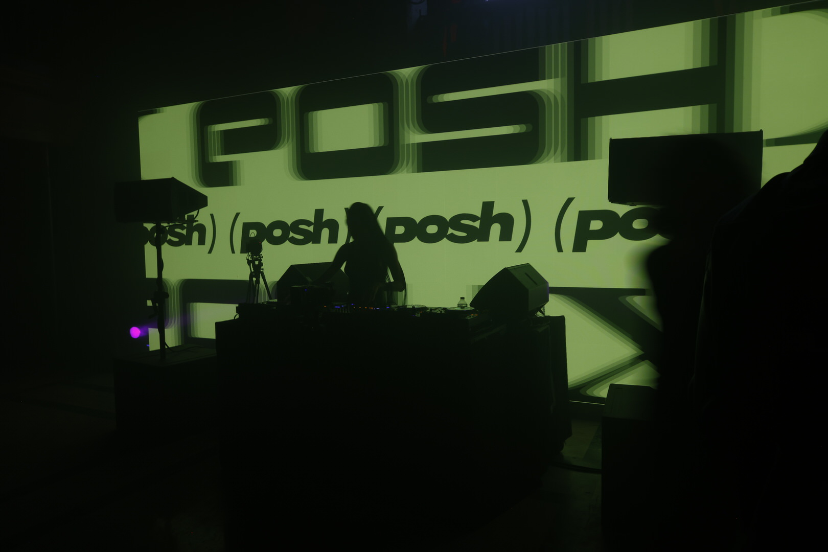 Silhouetted DJ performing behind decks against a large green Posh-branded backdrop