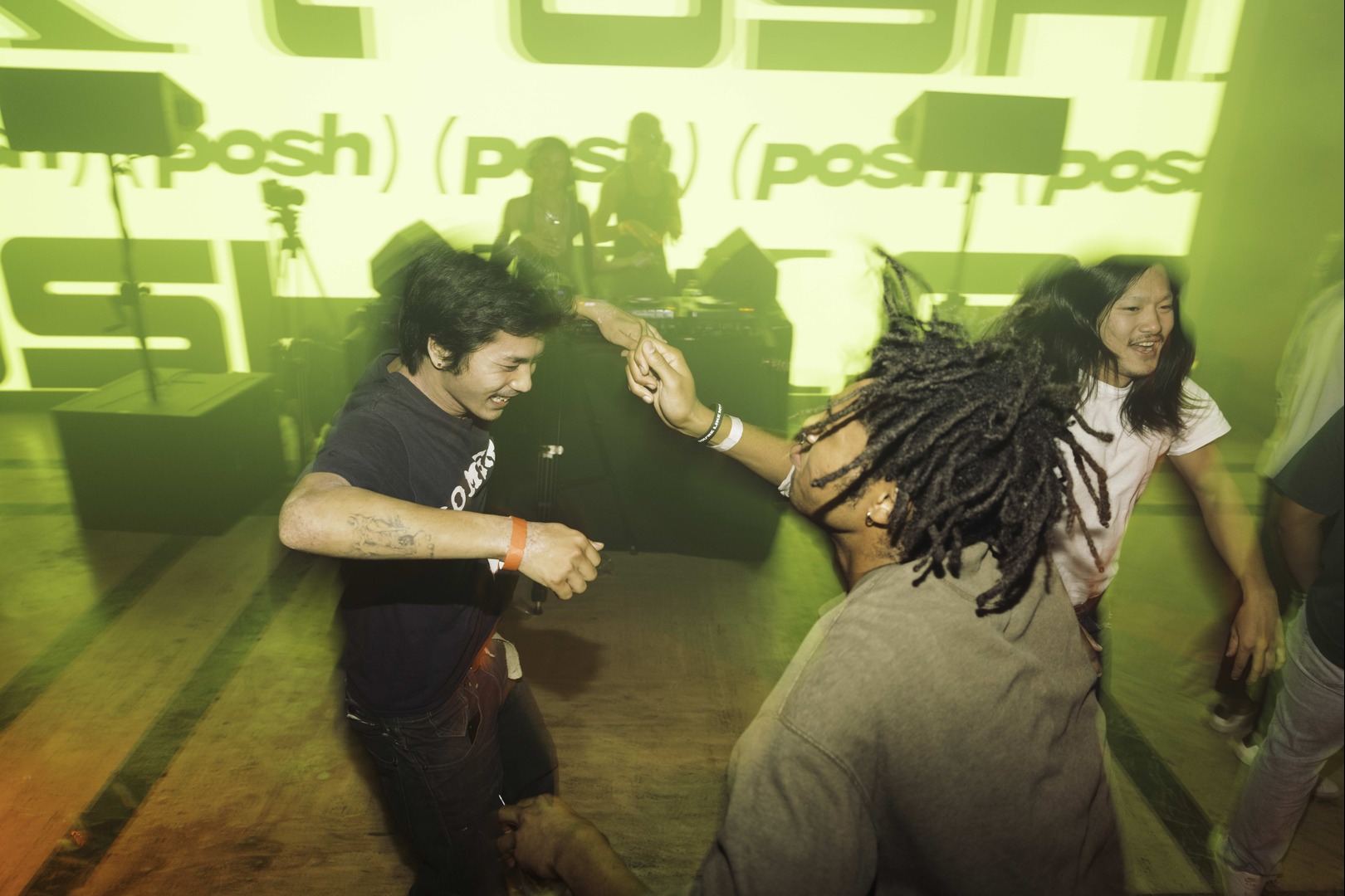 Two men laughing and dancing energetically before a green Posh-projected wall