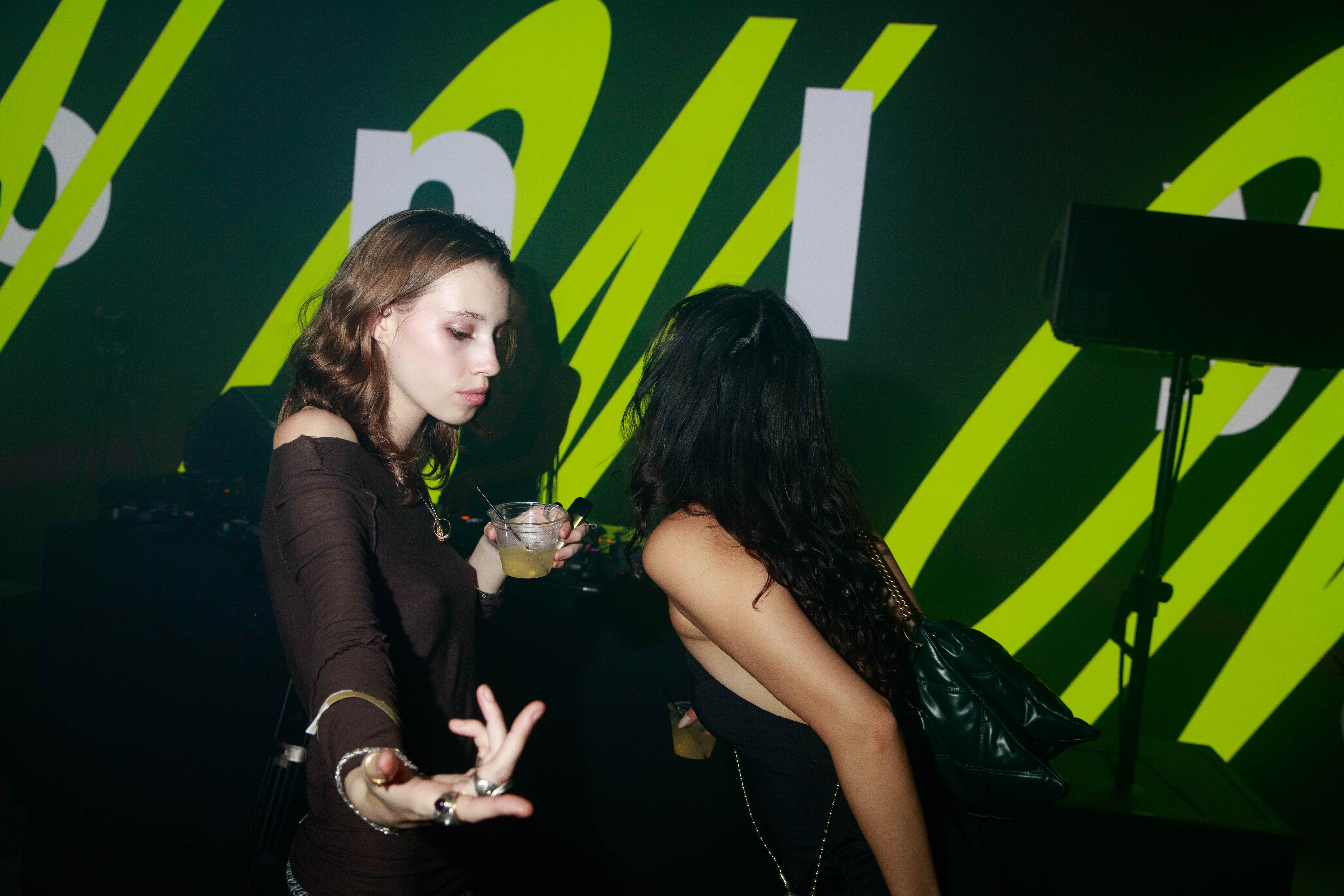 Two women dancing close at a club, one holding a cocktail, under green lighting