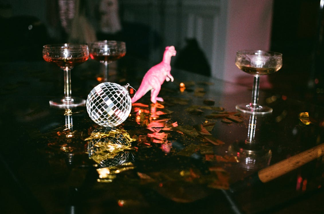Cocktail coupes, a pink toy dinosaur and a mini disco ball on a confetti-strewn table