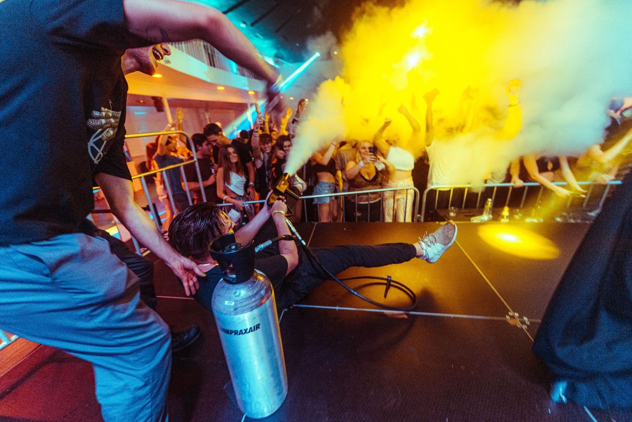 Crew member sprays a yellow CO2 cannon over a cheering crowd at a club