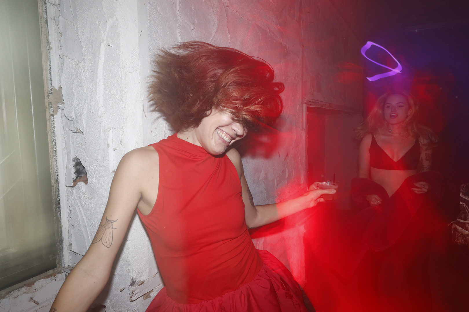 Woman in a red dress whips her hair laughing as another dances behind