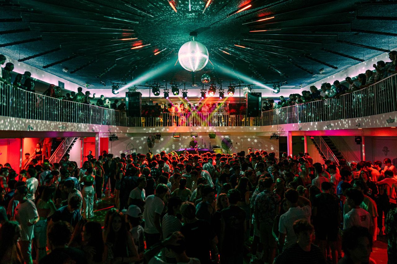 Packed two-tier nightclub crowd fills the floor beneath a spotlit stage