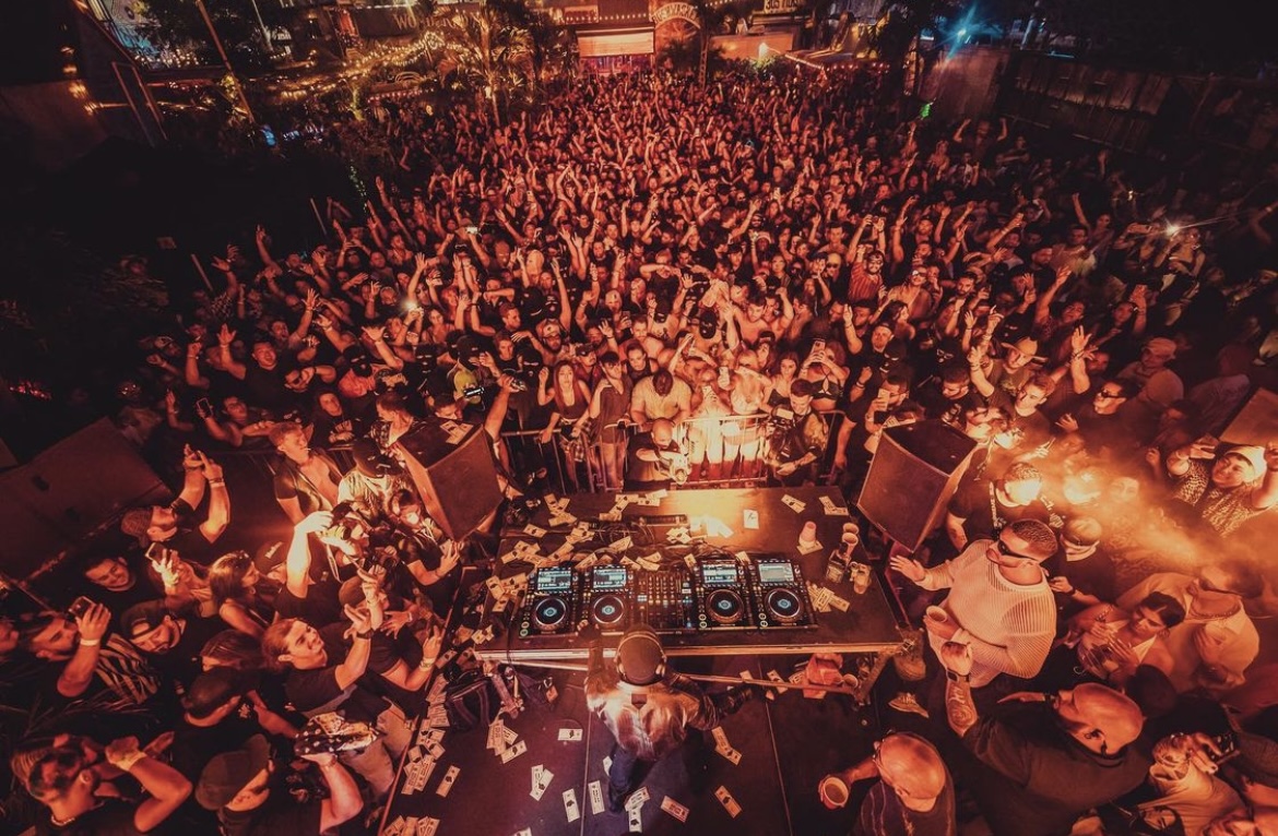 Aerial view of a massive packed outdoor crowd surrounding a DJ booth